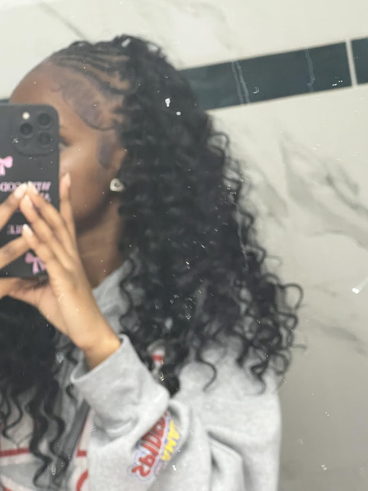Close up of a curly deep wave install with braided side sections, photographed in a bathroom mirror